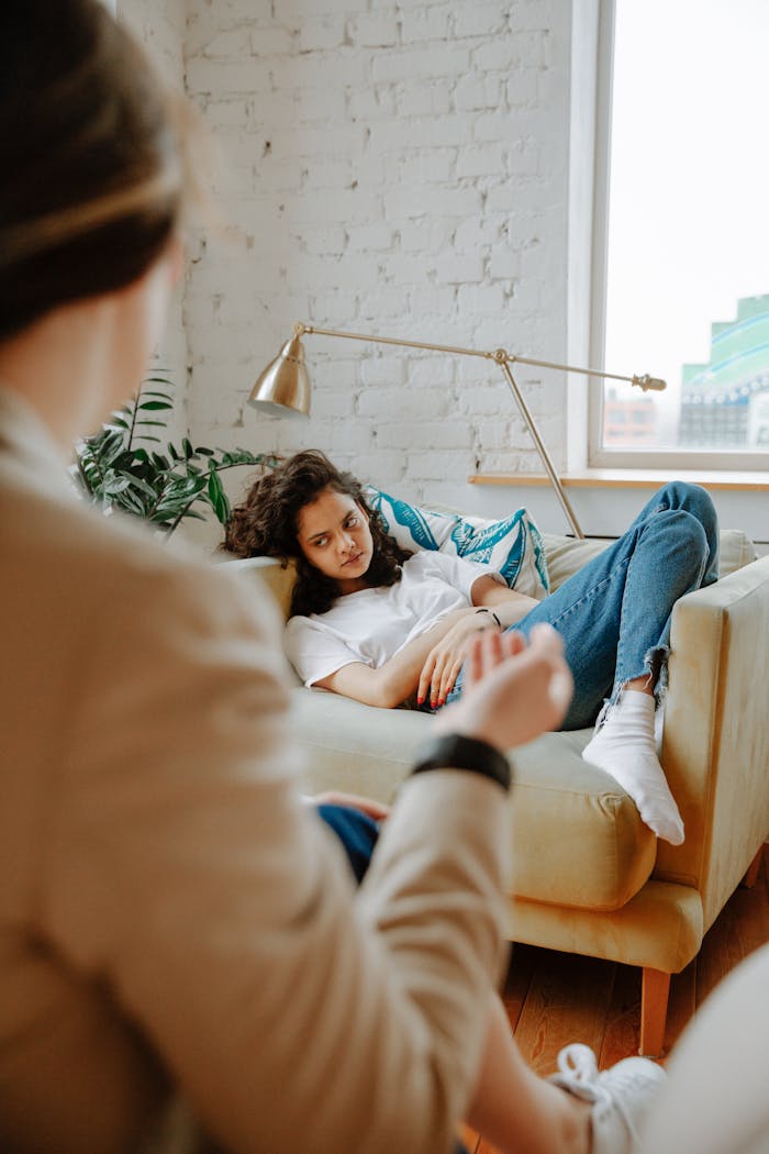 services-04 A therapist converses with a young adult on a sofa, focusing on mental health.
