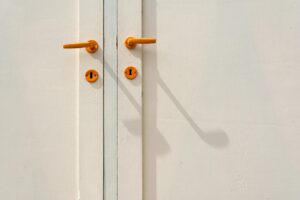 Minimalist close-up of a white door featuring orange handles and shadows, creating modern aesthetic.
